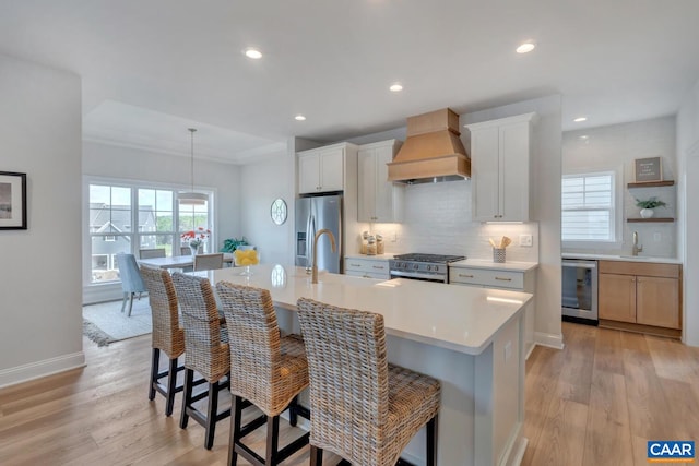 kitchen featuring white cabinets, a kitchen island with sink, and custom range hood