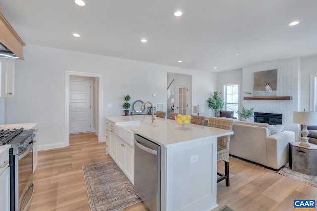 kitchen with light hardwood / wood-style flooring, a center island with sink, sink, stainless steel appliances, and a fireplace