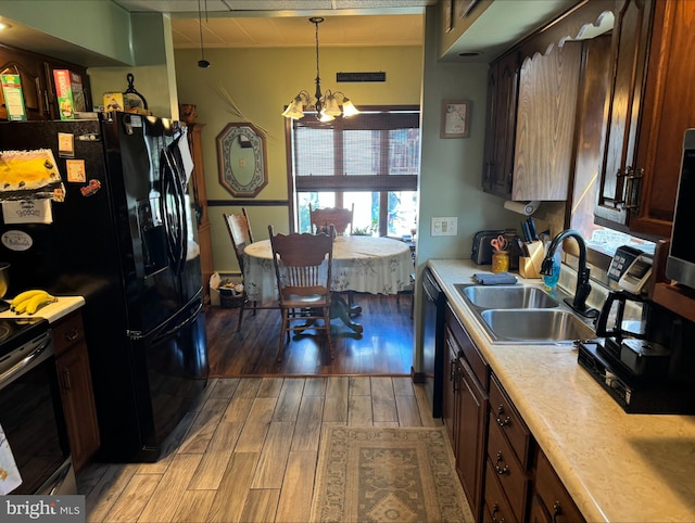 kitchen featuring black appliances, sink, hanging light fixtures, light hardwood / wood-style floors, and an inviting chandelier