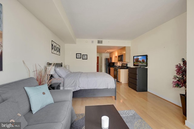 bedroom with black fridge and light hardwood / wood-style flooring