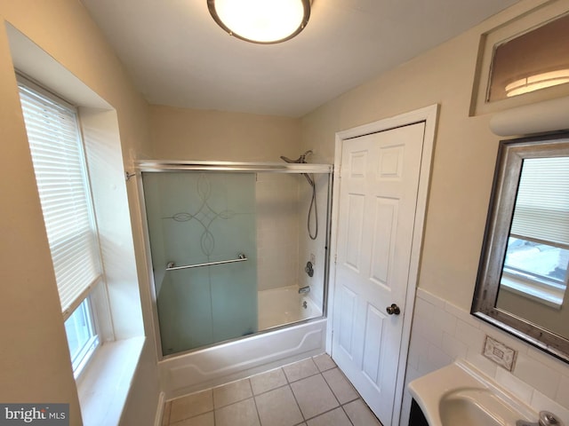 bathroom with tile patterned flooring, tile walls, shower / bath combination with glass door, and a wealth of natural light