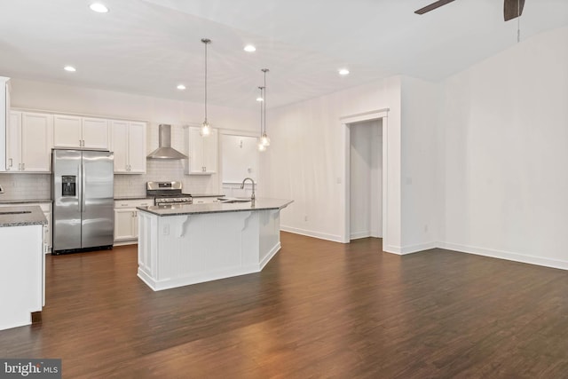 kitchen with an island with sink, stainless steel appliances, wall chimney exhaust hood, dark wood-type flooring, and white cabinetry