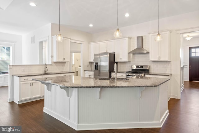 kitchen featuring wall chimney exhaust hood, a center island with sink, dark wood-type flooring, and appliances with stainless steel finishes