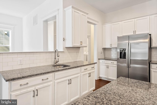 kitchen featuring sink, tasteful backsplash, stainless steel fridge with ice dispenser, white cabinetry, and dark stone counters