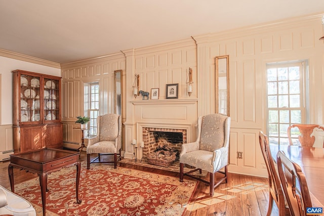 sitting room with a brick fireplace, crown molding, baseboard heating, and light hardwood / wood-style flooring