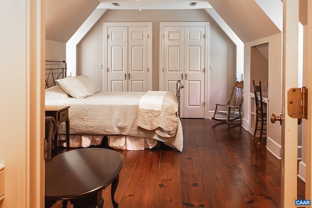 bedroom featuring two closets, dark wood-type flooring, and vaulted ceiling