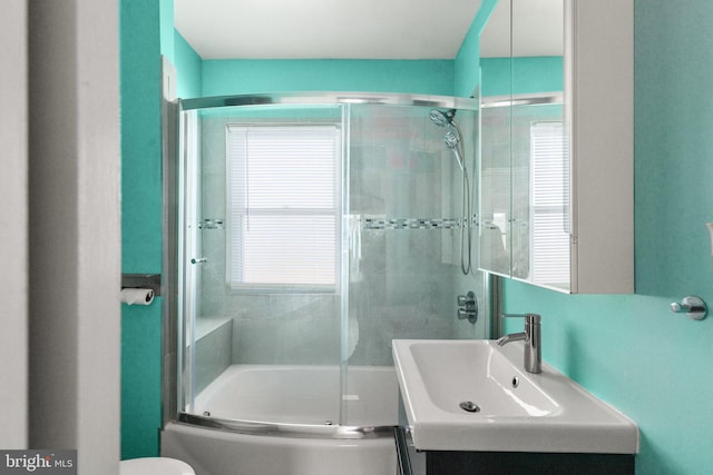 full bathroom featuring vanity, toilet, combined bath / shower with glass door, and a wealth of natural light