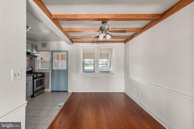 kitchen with beamed ceiling, stainless steel gas range, light tile patterned flooring, a textured ceiling, and ceiling fan