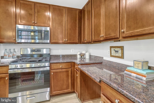 kitchen with dark stone countertops, stainless steel appliances, and light wood-type flooring