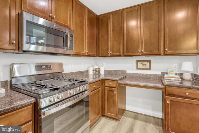 kitchen with light hardwood / wood-style floors, dark stone countertops, and appliances with stainless steel finishes