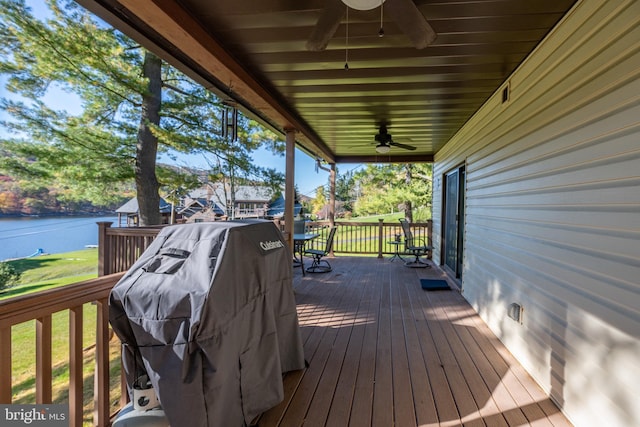 wooden terrace with a water view, ceiling fan, and a grill