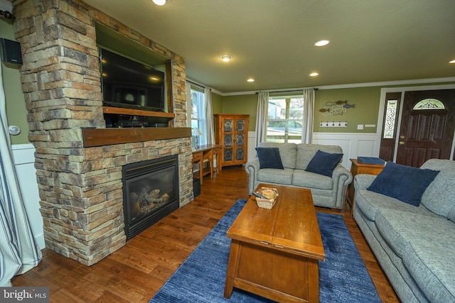 living room with crown molding, a stone fireplace, and dark hardwood / wood-style flooring