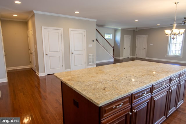 kitchen with hanging light fixtures, light stone countertops, ornamental molding, dark wood-type flooring, and a center island