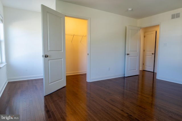 unfurnished bedroom featuring a closet, dark hardwood / wood-style floors, and a walk in closet