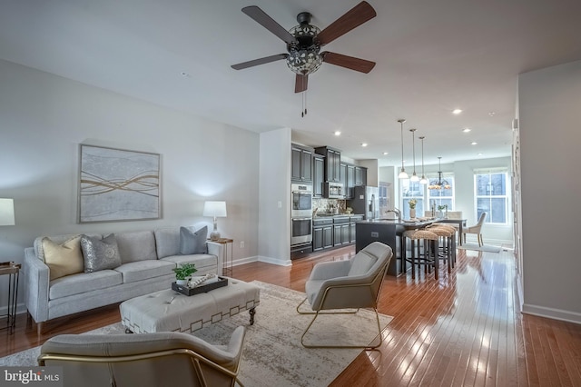 living room with sink, ceiling fan with notable chandelier, and light wood-type flooring