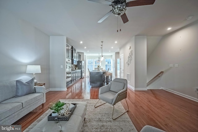 living room with ceiling fan with notable chandelier and hardwood / wood-style floors