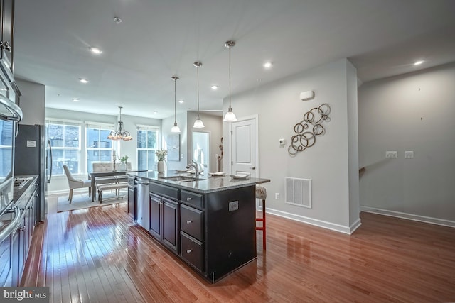 kitchen with sink, a kitchen bar, pendant lighting, hardwood / wood-style flooring, and a center island with sink