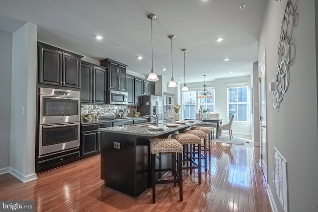 kitchen featuring light wood-type flooring, stainless steel appliances, pendant lighting, a breakfast bar area, and a kitchen island with sink