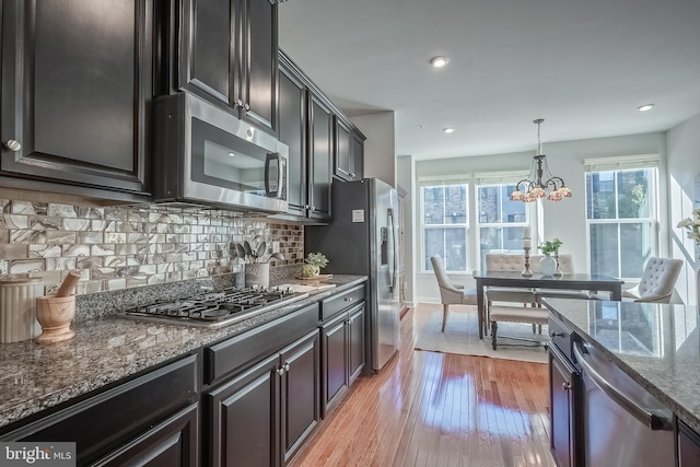 kitchen featuring tasteful backsplash, appliances with stainless steel finishes, light wood-type flooring, hanging light fixtures, and dark stone countertops