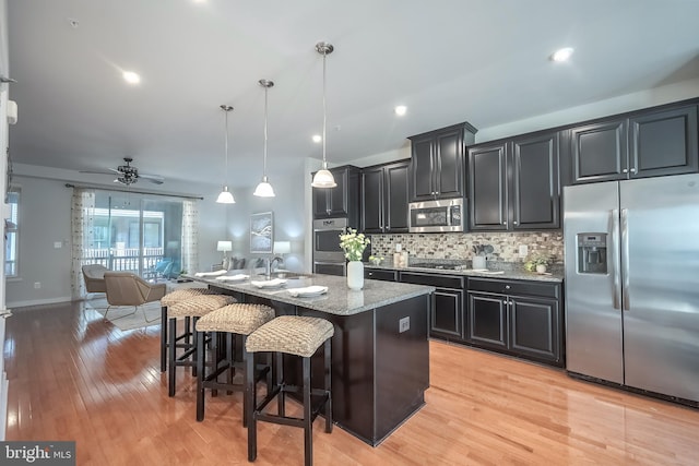 kitchen with an island with sink, appliances with stainless steel finishes, a kitchen breakfast bar, pendant lighting, and light hardwood / wood-style floors