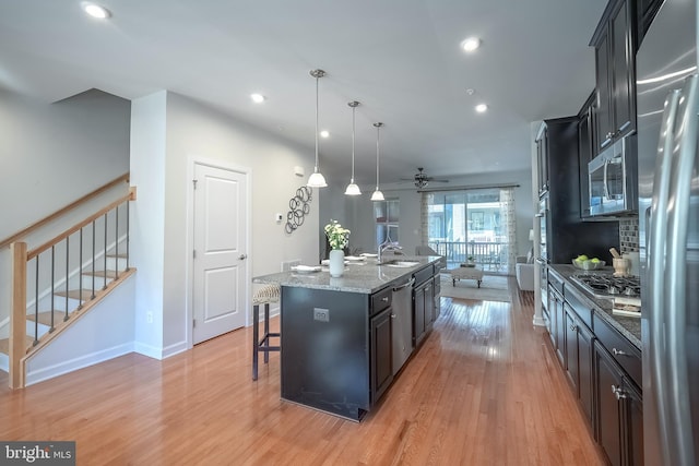 kitchen with appliances with stainless steel finishes, hanging light fixtures, light hardwood / wood-style floors, a breakfast bar, and a center island with sink