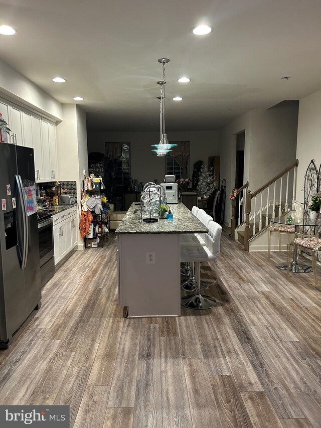 kitchen with light hardwood / wood-style floors, pendant lighting, light stone counters, appliances with stainless steel finishes, and white cabinetry