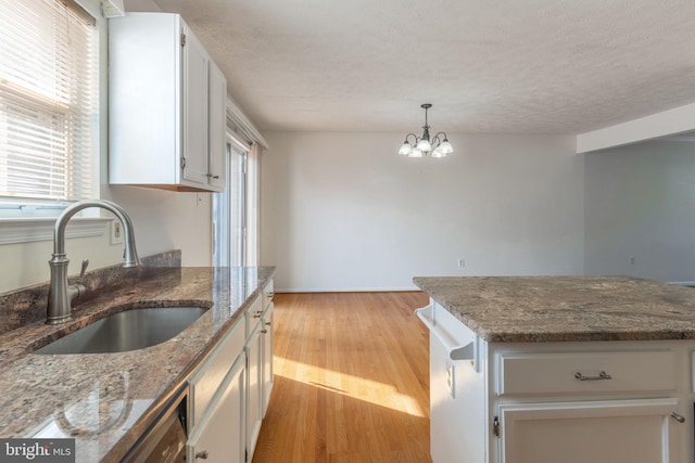 kitchen with sink, a chandelier, dark stone counters, white cabinetry, and light wood-type flooring