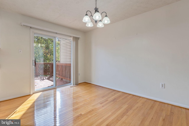 unfurnished room featuring an inviting chandelier, light hardwood / wood-style flooring, and a textured ceiling