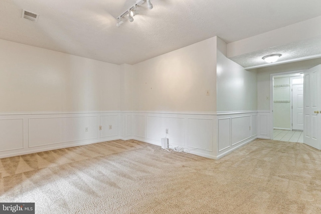 carpeted empty room with rail lighting and a textured ceiling