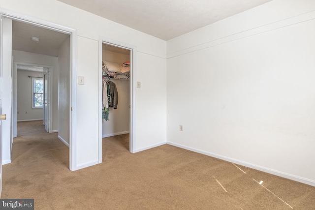 unfurnished bedroom featuring a closet, light colored carpet, and a walk in closet