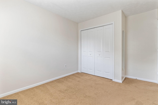 unfurnished bedroom featuring light carpet, a textured ceiling, and a closet