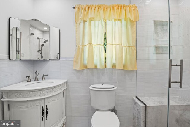 bathroom with tile walls, vanity, toilet, and tiled shower