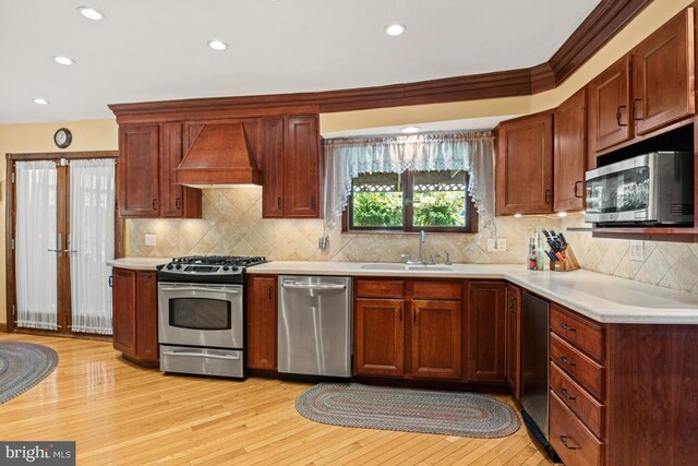 kitchen with premium range hood, light hardwood / wood-style flooring, ornamental molding, sink, and stainless steel appliances