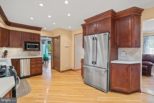 kitchen featuring crown molding, appliances with stainless steel finishes, light hardwood / wood-style flooring, and backsplash