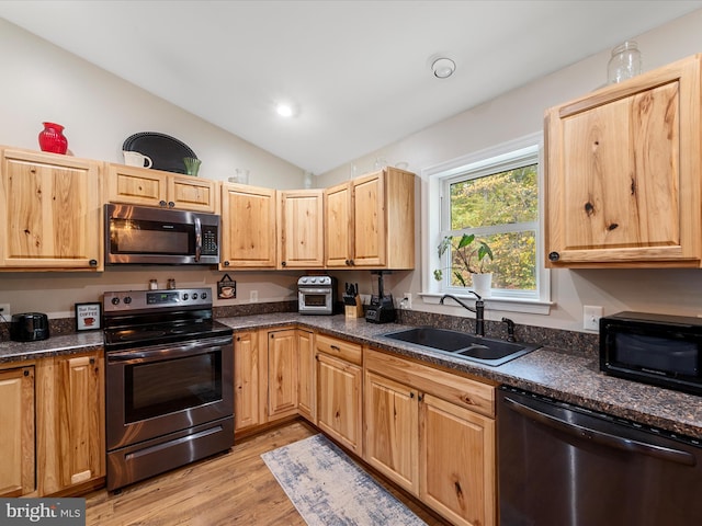 kitchen featuring lofted ceiling, stainless steel appliances, dark stone countertops, sink, and light hardwood / wood-style floors