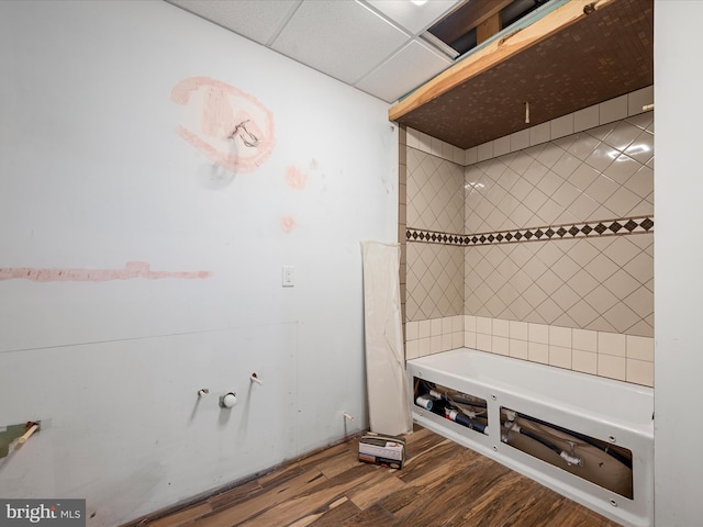 bathroom with a drop ceiling, hardwood / wood-style flooring, and a washtub