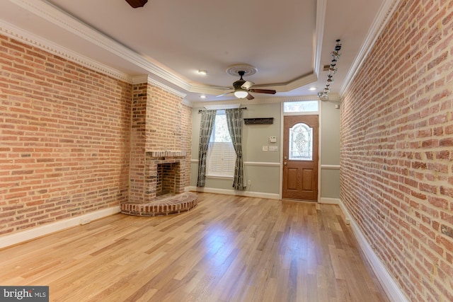 unfurnished living room featuring brick wall, hardwood / wood-style floors, crown molding, a brick fireplace, and ceiling fan