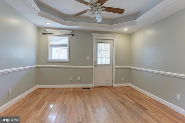 interior space with ornamental molding, a tray ceiling, light wood-type flooring, and ceiling fan