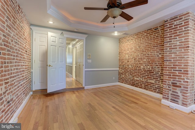 unfurnished room with light hardwood / wood-style floors, brick wall, and a tray ceiling