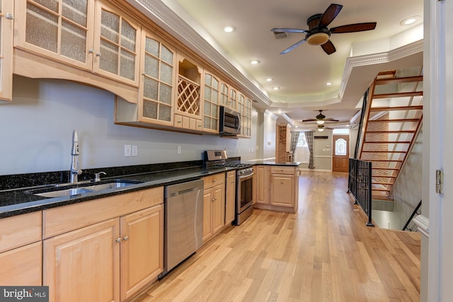 kitchen with light brown cabinets, stainless steel appliances, dark stone countertops, sink, and light hardwood / wood-style floors