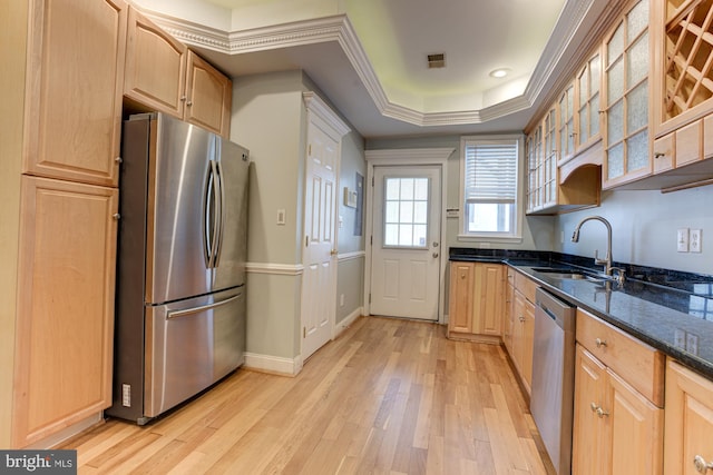 kitchen with stainless steel appliances, dark stone countertops, sink, light wood-type flooring, and a raised ceiling