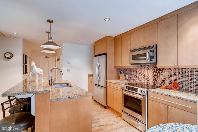 kitchen with light stone countertops, sink, stainless steel appliances, pendant lighting, and light hardwood / wood-style flooring