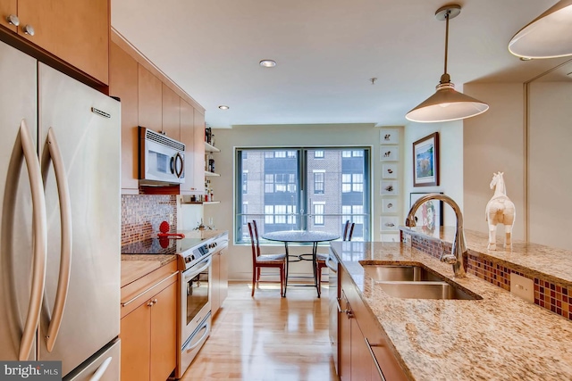 kitchen with appliances with stainless steel finishes, sink, hanging light fixtures, decorative backsplash, and light hardwood / wood-style flooring