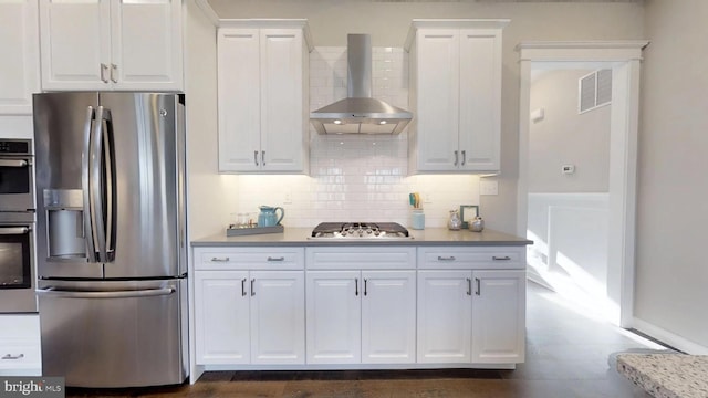 kitchen with appliances with stainless steel finishes, wall chimney range hood, white cabinetry, and tasteful backsplash