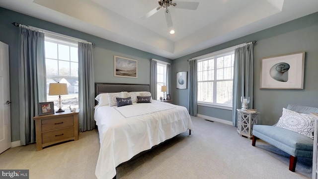 carpeted bedroom with a raised ceiling, multiple windows, and ceiling fan