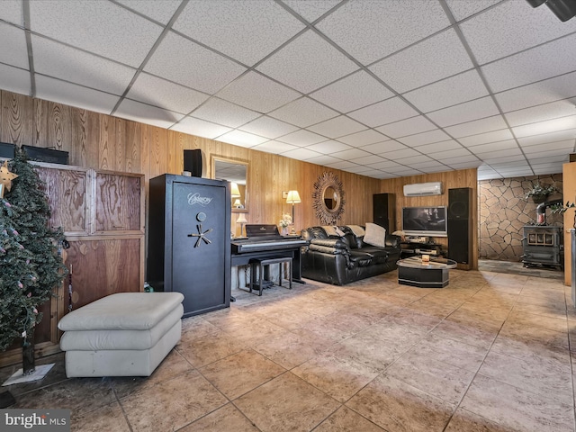 living room featuring wooden walls, a drop ceiling, a wall mounted air conditioner, and a wood stove