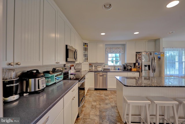 kitchen with dark stone counters, a breakfast bar, sink, white cabinets, and appliances with stainless steel finishes