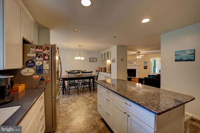 kitchen with a center island, white cabinets, dark stone countertops, ceiling fan with notable chandelier, and pendant lighting