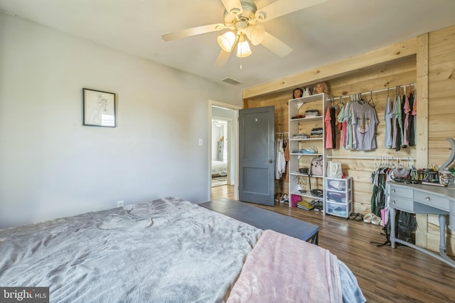 bedroom featuring wood walls, dark hardwood / wood-style floors, a closet, and ceiling fan