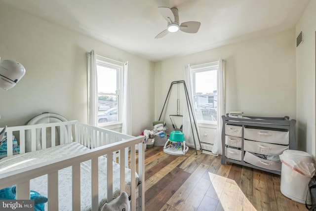 bedroom with hardwood / wood-style floors, multiple windows, a crib, and ceiling fan